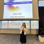 An 18-year old girl stands with an award in a large ballroom. The sign above her reads National Philanthropy Day